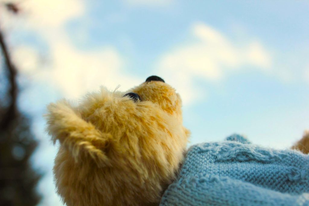 A photo of a teddy bear lying on its back, looking up at the bright blue sky. 